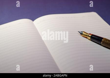 Close view of the tip of a pen writing on an open agenda or notebook with blank pages. Writing on paper with pen ink. Blue surface, wallpaper or deskt Stock Photo