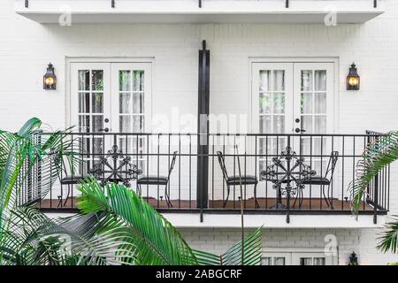 A set of balconies on a white building with tables and chairs sitting in front of the doors and trees outside. Stock Photo