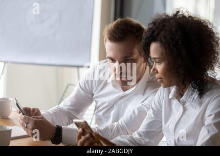 Multiethnic colleagues use cellphones try smartphone applications in office Stock Photo