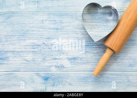 Rolling pin and heart shaped cookie cutter on blue wooden background with copy space Stock Photo