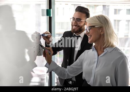 Smiling diverse colleagues brainstorm in office writing on bard Stock Photo