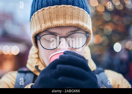 Young man with foggy up eyeglasses drinking hot wine. Christmas market in Tallinn, Estonia. Stock Photo