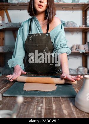 Cropped Photo of Young Attractive Woman Dressed In Green Stylish Apron Holding Rolling Pin and Making Clay Dish. Stock Photo