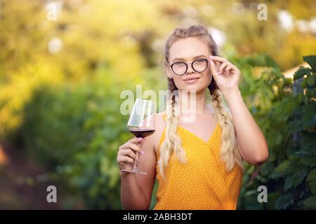 Portrait of a beautiful blonde woman wearing glasses enjoying a glass of red wine. Alone female posing and making a toast outdoors Stock Photo