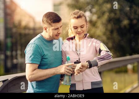 Smiling couple checking time or pulse on heart rate monitor watch - Runners in the park - Man and woman training outside in nature Stock Photo