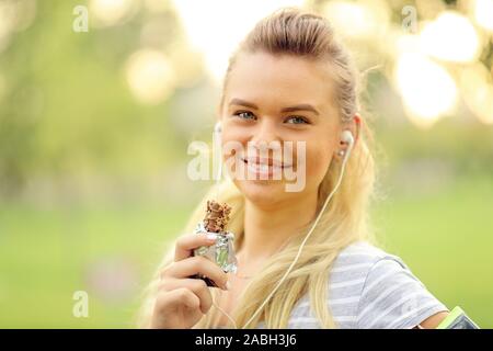 Athletic woman eating a protein bar - Closeup portrait of smiling young sporty girl posing while resting and grabbing a nutritive bar Stock Photo