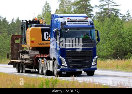 Blue Volvo FH 500 semi trailer of Santalan Betoni Oy hauls Cat tracked excavator along Finnish highway 25 in summer. Raasepori, Finland. July 12, 2019 Stock Photo