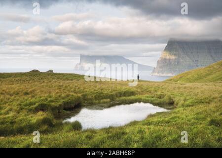 Lonely tourist near small lake looks at foggy islands in Atlantic ocean from Kalsoy island, Faroe Islands, Denmark. Landscape photography Stock Photo