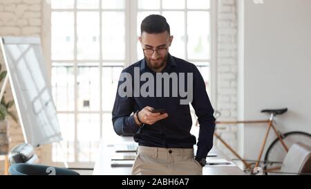 Pleasant millennial arabic businessman using smartphone at modern workplace. Stock Photo