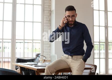 Worried millennial arabic male employee talking on cellular phone. Stock Photo