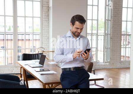 Smiling confident office manager using cellphone, enjoying break time. Stock Photo