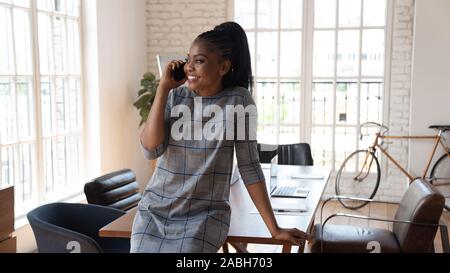 Happy millennial african american female manager talking on mobile phone. Stock Photo