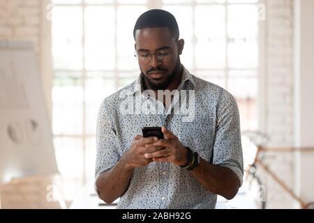 Serious african american young employee using smartphone. Stock Photo