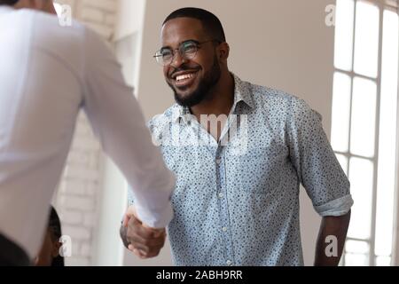 Joyful african american millennial worker shaking hands with colleague. Stock Photo