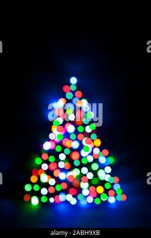 Glowing and festive colored light circles created from in camera and lens bokeh. Christmas fairy lights defocused giving a blurred effect. Background Stock Photo
