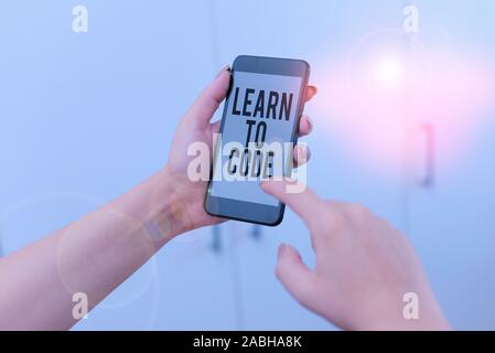 Word writing text Learn To Code. Business photo showcasing Learn to write Software Be a Computer Programmer Coder woman using smartphone office suppli Stock Photo