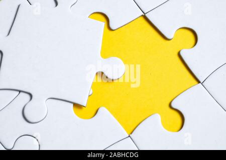 Missing white piece lies on jigsaw puzzle on yellow background. Concept of completing the final puzzle piece, achieving goal. Stock Photo