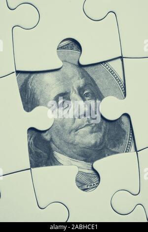Image on 100 U.S. dollar bill image opened under the white jigsaw puzzle. Concept of hidden finance, double-entry bookkeeping, money stash. Vertical. Stock Photo