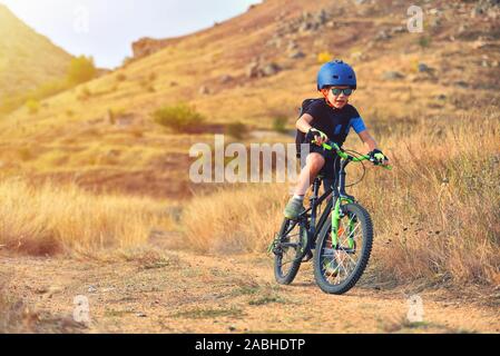 Happy kid boy of 7 years having fun in autumn park with a bicycle on beautiful fall day. Active child wearing bike helmet Stock Photo