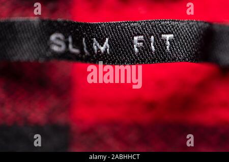 Label on a Red Shirt Indicating the Size of Clothes- Slim Fit. Red Garment Background Stock Photo