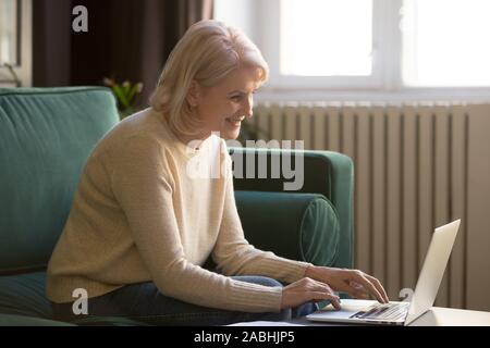 Elderly woman sitting on couch typing on computer Stock Photo