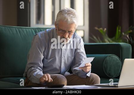 Mature man holding receipt calculates on calculator monthly expenses Stock Photo