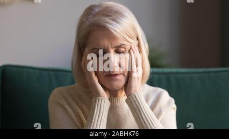 Closeup portrait aged woman touches temples suffers from migraine Stock Photo