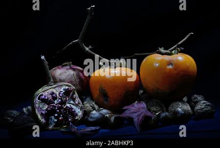 persimmon, pomegranate whole and open-face and walnuts on a black background Stock Photo
