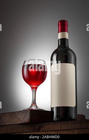Blank beige label on the bottle of red wine and wineglass on the wooden table. Wine bottle mockup. Stock Photo