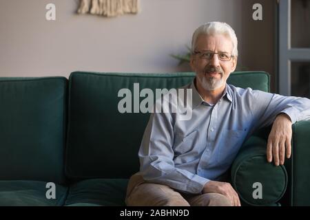 Single handsome elderly man sitting on couch looking at camera Stock Photo