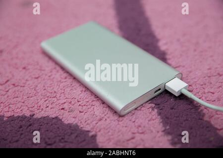 Energy bank . Smartphone Charging with silver Power Bank Through Spiral USB Cable . Smartphone charging with power bank on pink carpet . Stock Photo