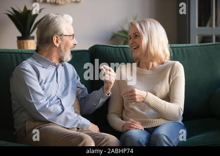 Cheerful elderly spouses sitting on couch chatting feel happy Stock Photo