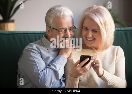Mature attractive couple sitting on couch using smartphone Stock Photo