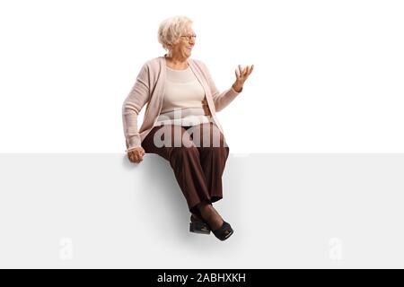 Elderly woman sitting on a panel looking to the side and gesturing with hand isolated on white background Stock Photo