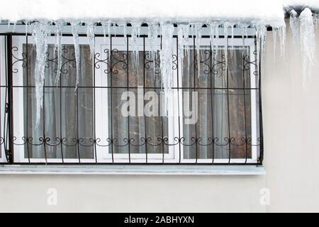 Frozen ice hanging over the window of a residential building with windows on the balcony is dangerously humiliated by passersby. Icicles over the wind Stock Photo