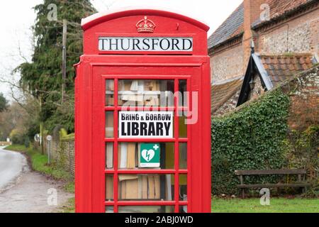 red telephone phone box being used as a local library and defibrillator point, Thursford, Norfolk, England, UK Stock Photo