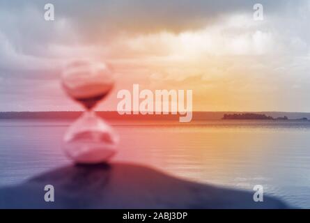 Blurred hourglass on a rock, illuminated in red as a concept of lost time. Stock Photo