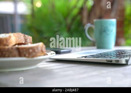 Working on the computer and cell phone while having breakfast. Work from home or flexi time concept. Stock Photo