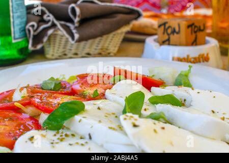 A colorful caprese salad, basket of bread and bottle of water on a table in an outdoor sidewalk cafe in Brindisi Italy. Stock Photo
