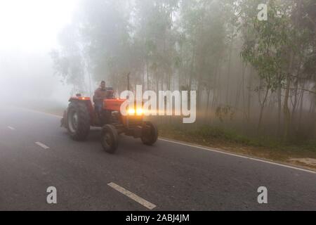 Bangladesh – January 06, 2014: On a foggy winter morning, a tractor is passing through the foggy streets at Ranisankail, Thakurgaon. Stock Photo