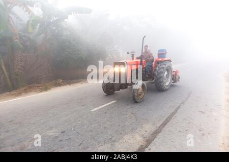 Bangladesh – January 06, 2014: On a foggy winter morning, a tractor is passing through the foggy streets at Ranisankail, Thakurgaon. Stock Photo