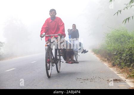 Bangladesh – January 06, 2014: On a foggy winter morning, some village people going to work on a bicycle through the foggy streets at Ranisankail, Tha Stock Photo