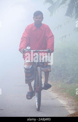 Bangladesh – January 06, 2014: On a foggy winter morning, some village people going to work on a bicycle through the foggy streets at Ranisankail, Tha Stock Photo