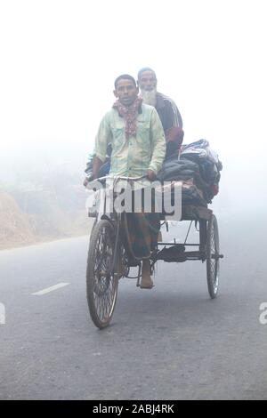 Bangladesh – January 06, 2014: On a foggy winter morning, some village people going to work on a bicycle through the foggy streets at Ranisankail, Tha Stock Photo