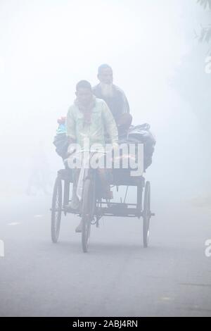 Bangladesh – January 06, 2014: On a foggy winter morning, some village people going to work on a bicycle through the foggy streets at Ranisankail, Tha Stock Photo