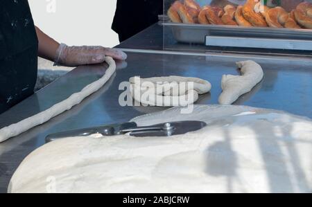 A baker rolls raw dough into a rope to make a hot, soft pretzel fresh from the oven Stock Photo