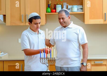 Happy family is lighting a candle celebrating together Jewish holiday Hanukkah. Jewish Dad and teenager son or grandfather with grandson lighting Chanukkah Candles in a menorah for the holdiay Stock Photo