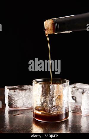 coffee liquor poring in glass with ice cubes isolated on black