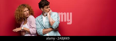 beautiful skeptical couple in casual clothes isolated on red Stock Photo