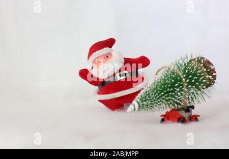 Toy Santa Claus on background blurred toy car carrying Christmas tree. Simulated snowy landscape. Space for text Stock Photo